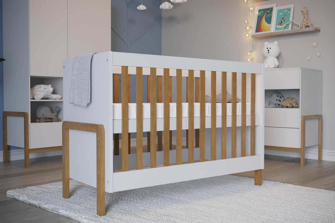 A modern baby crib with a white frame and natural light oak wood slats and legs, shown on a plain white background.