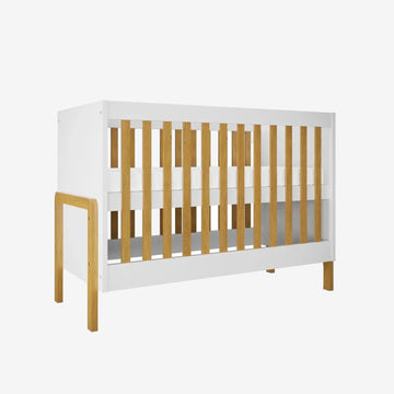 A modern baby crib with a white frame and natural light oak wood slats and legs, shown on a plain white background.